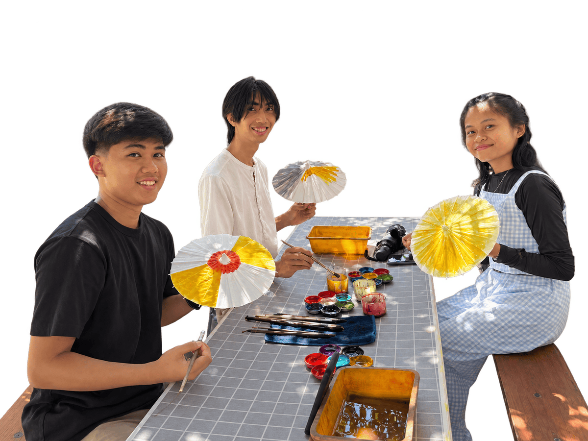 三位學生圍著桌子一起彩繪黃色紙傘