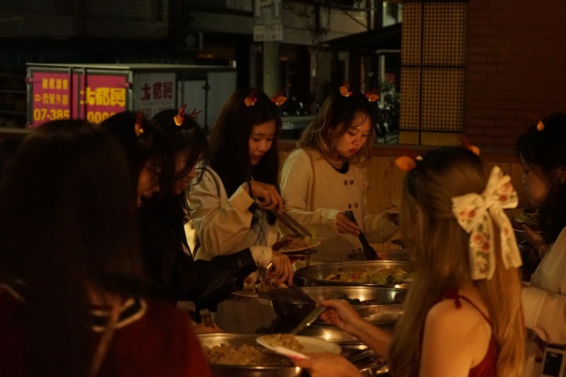 大家圍在餐點區享用美食，在溫馨燈光下共享歡樂聖誕時光。🍽️🎄✨圖片
